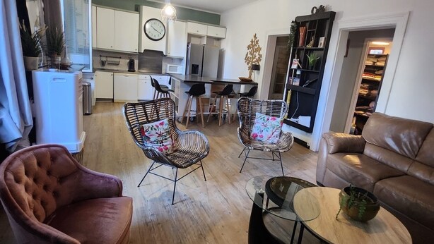 A modern living room with a brown leather sofa, wicker chairs, a glass coffee table, and a dining area with a white table and chairs. - Logement Entier à Proximité des Plages et Commerces (Sète)