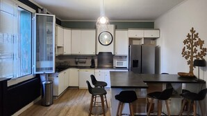 A modern kitchen with a central island, bar stools, a clock, and a decorative tree on the wall. - Logement Entier à Proximité des Plages et Commerces (Sète)