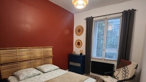 A bedroom with two beds, a bedside table, a chair, a window with curtains, and a hanging light fixture. - Logement Entier à Proximité des Plages et Commerces (Sète)