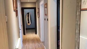 A hallway with wooden flooring, white walls, and framed pictures. There is a door at the end of the hallway. - Logement Entier à Proximité des Plages et Commerces (Sète)