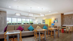 A modern hotel lobby with a sofa, tables, chairs, and a reception desk. - Home2 Suites by Hilton Vero Beach I-95 (Vero Beach)