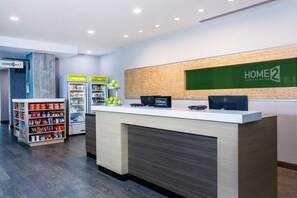 A hotel reception area with a counter, vending machines, and a display for 'HOME 2' branded products. - Home2 Suites by Hilton Vero Beach I-95 (Vero Beach)