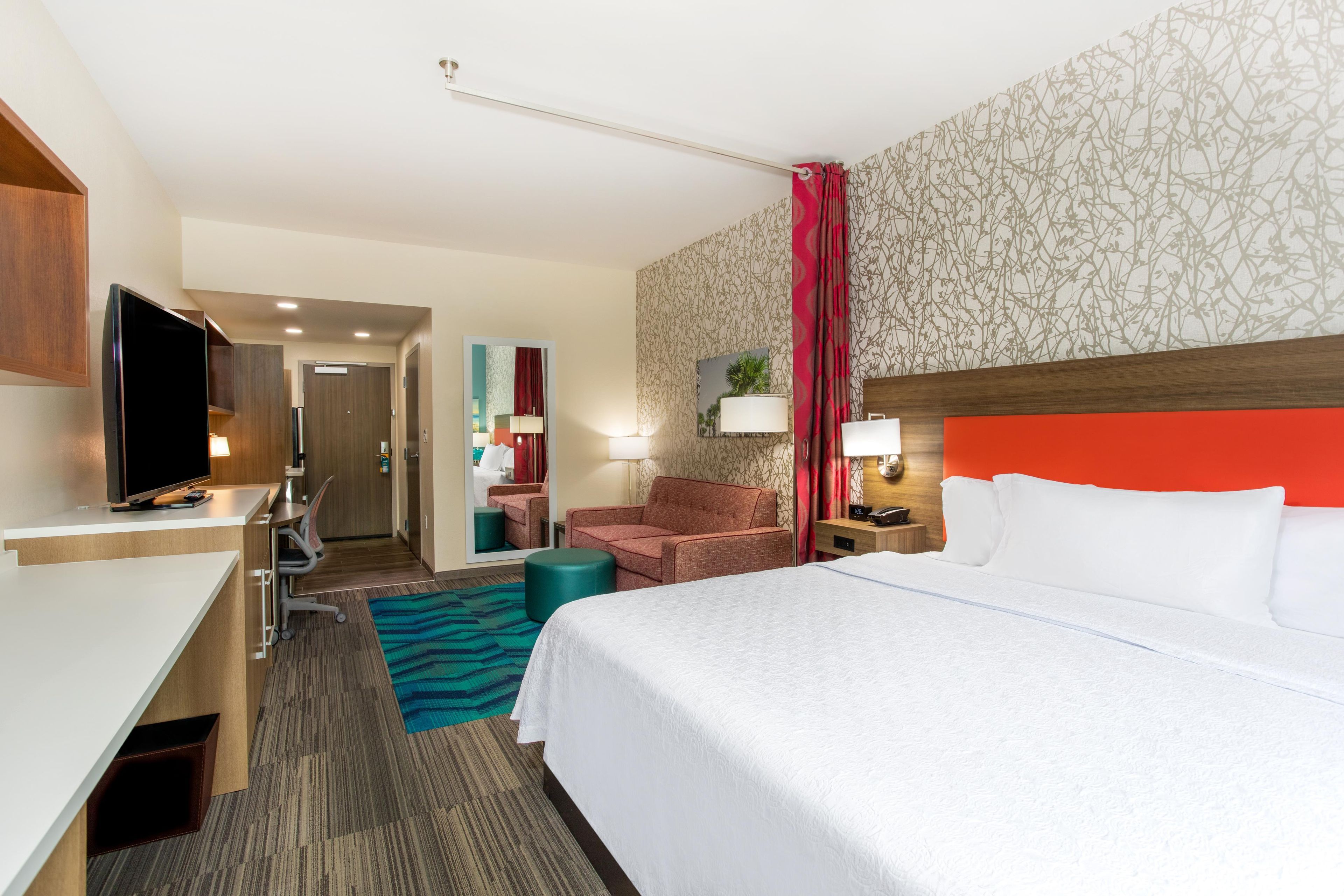 Habitación de hotel con cama, escritorio, televisor, silla, mesita de noche y baño visible a través de una puerta abierta.