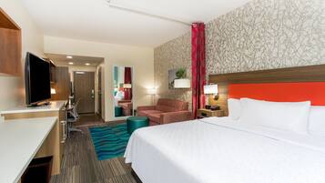Habitación de hotel con cama, escritorio, televisor, silla, mesita de noche y baño visible a través de una puerta abierta.
