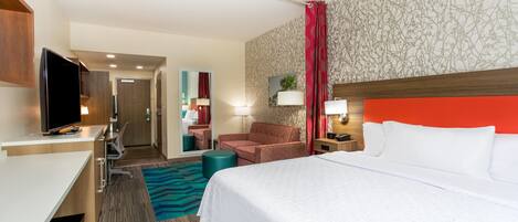 A hotel room with a bed, a desk, a television, a chair, a nightstand, and a bathroom visible through an open door.