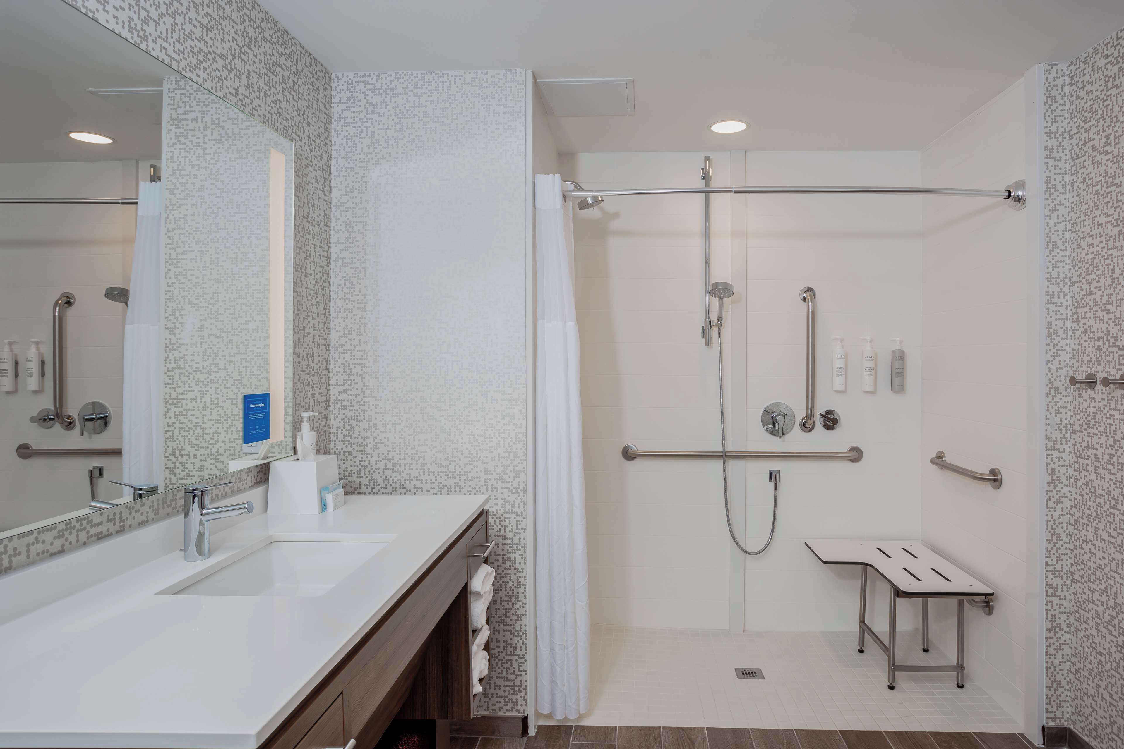 Une salle de bain moderne avec deux lavabos, une douche équipée de barres d’appui et un miroir.