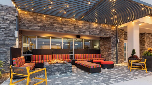 An outdoor seating area with stone walls, a fire feature, and modern furniture. - Home2 Suites by Hilton Vero Beach I-95 (Vero Beach)