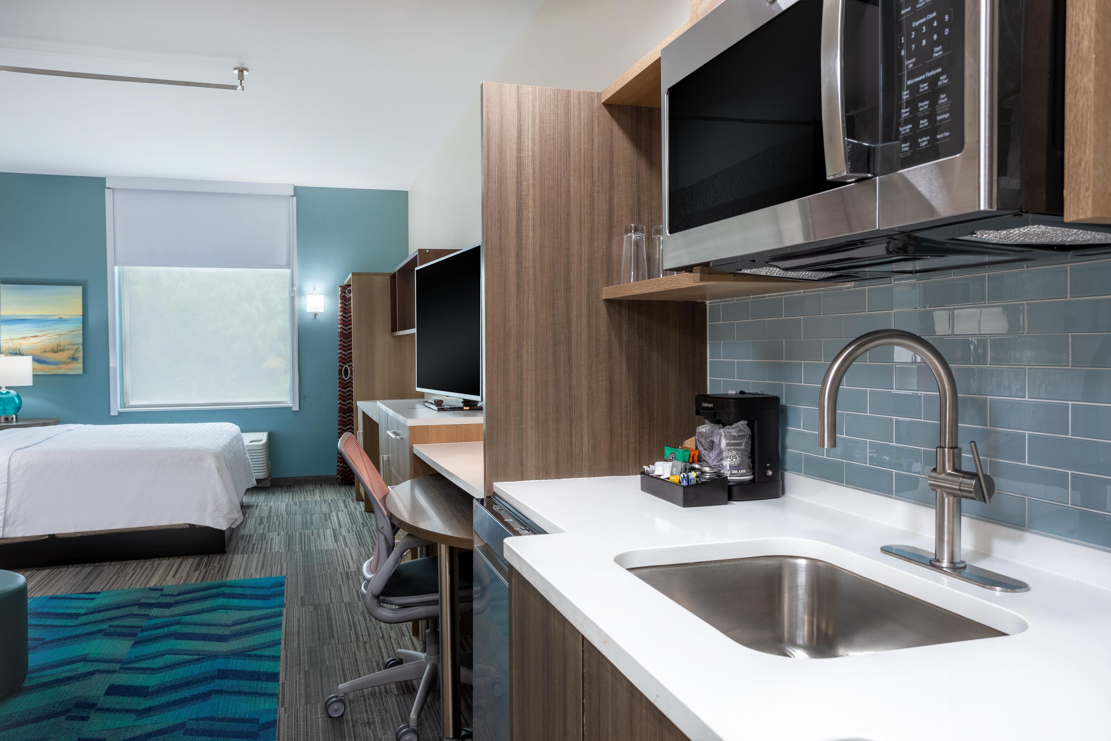 Een compacte hotelkamer met kitchenette, een bed, een bureau en uitzicht op de omgeving.