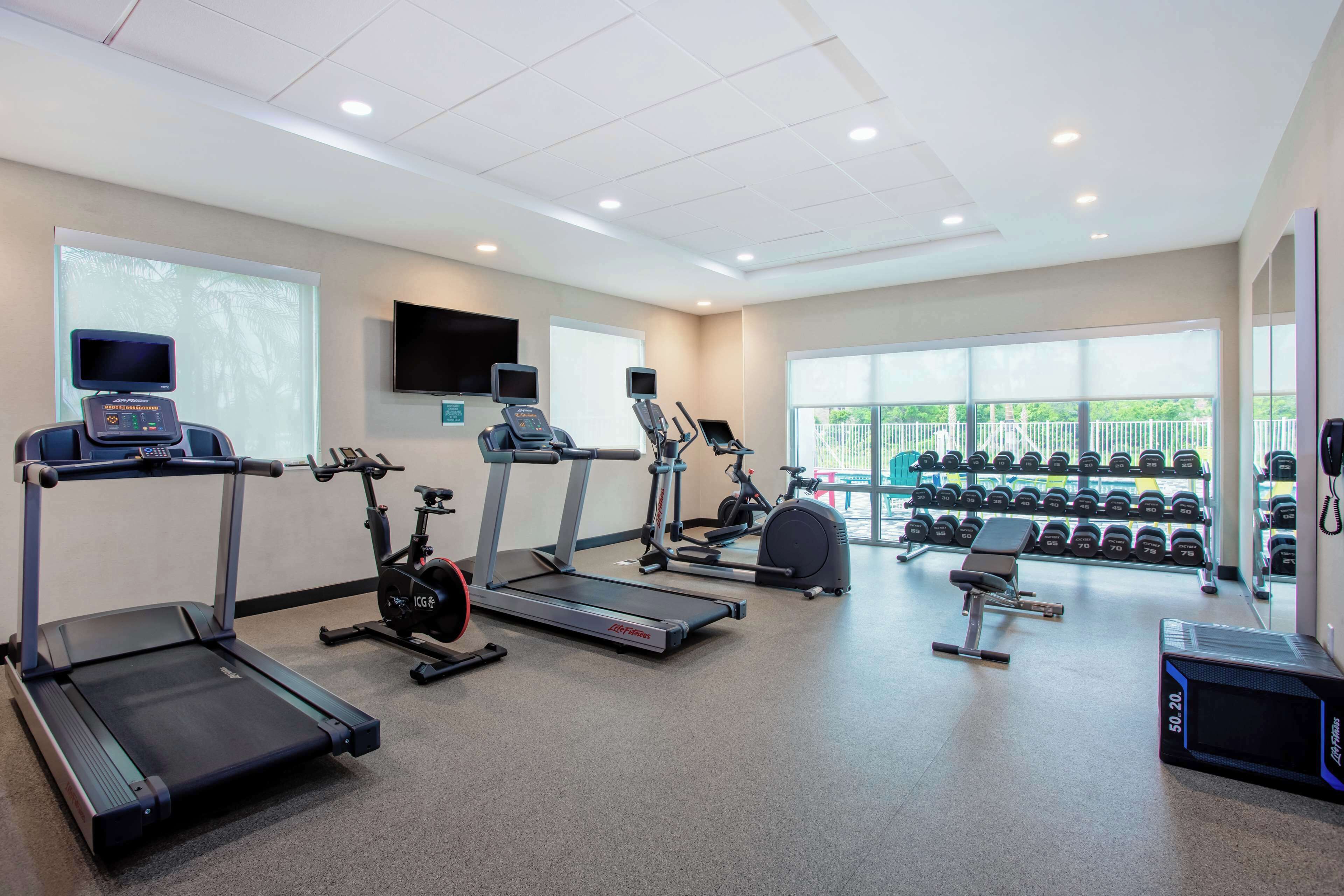 Un gimnasio con cintas de correr, elípticas, bicicletas estáticas y una variedad de mancuernas.