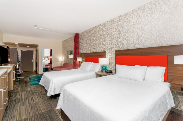 A hotel room with two beds, a desk, a TV, and a bathroom.