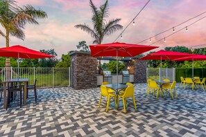 An outdoor patio area with a stone barbecue station, yellow chairs, and red umbrellas. - Home2 Suites by Hilton Vero Beach I-95 (Vero Beach)