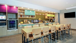 A modern restaurant with a long wooden table and chairs, a counter with a menu, and a television screen. - Home2 Suites by Hilton Vero Beach I-95 (Vero Beach)
