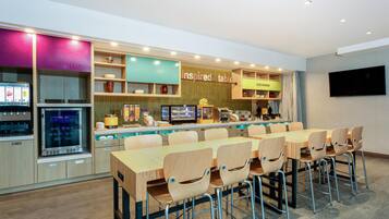 Ein modernes Restaurant mit einem langen Holztisch und Stühlen, einer Theke mit einer Kaffeemaschine und einem an der Wand befestigten Fernseher.
