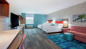 A hotel room with a TV, two beds, a sofa, and a patterned carpet. - Home2 Suites by Hilton Vero Beach I-95 (Vero Beach)
