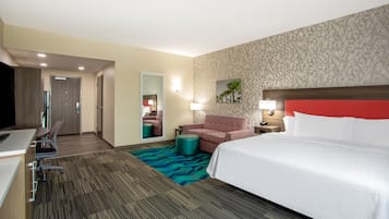 A hotel room with a bed, a desk, a chair, a sofa, and a small table.