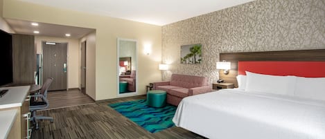 A hotel room with a bed, a desk, a chair, a sofa, and a small table.