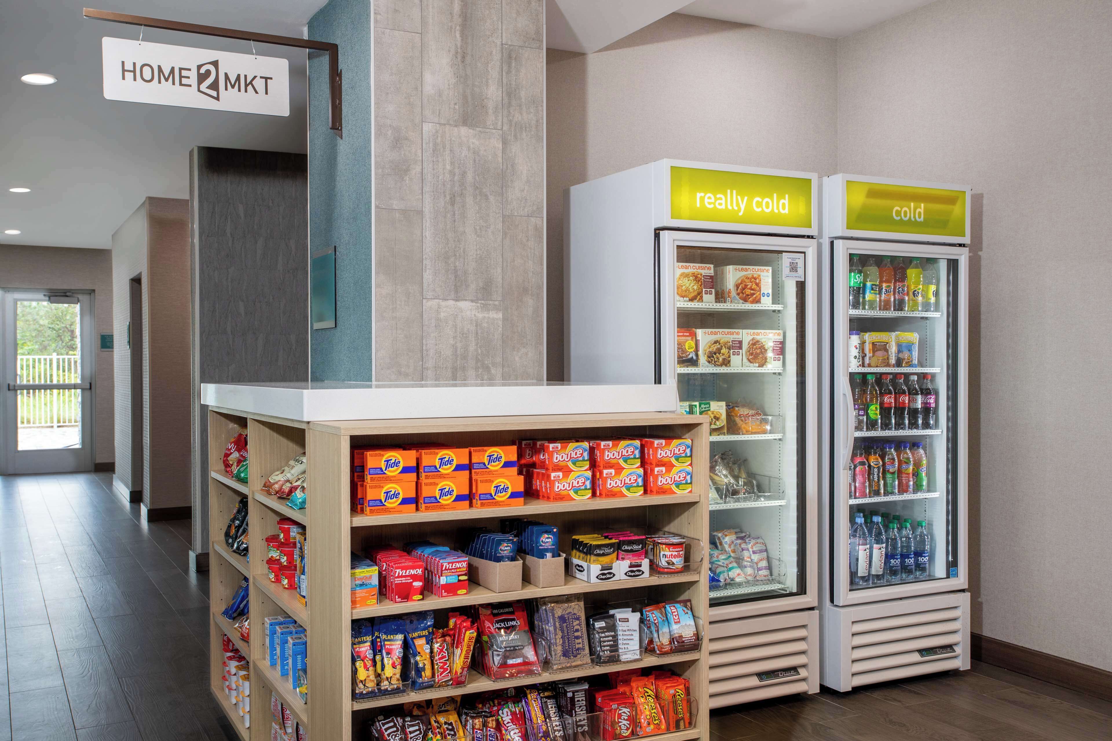 A hotel lobby with a self-service snack area, including shelves stocked with various snacks and two refrigerated beverage dispensers labeled "really cold" and "cold".