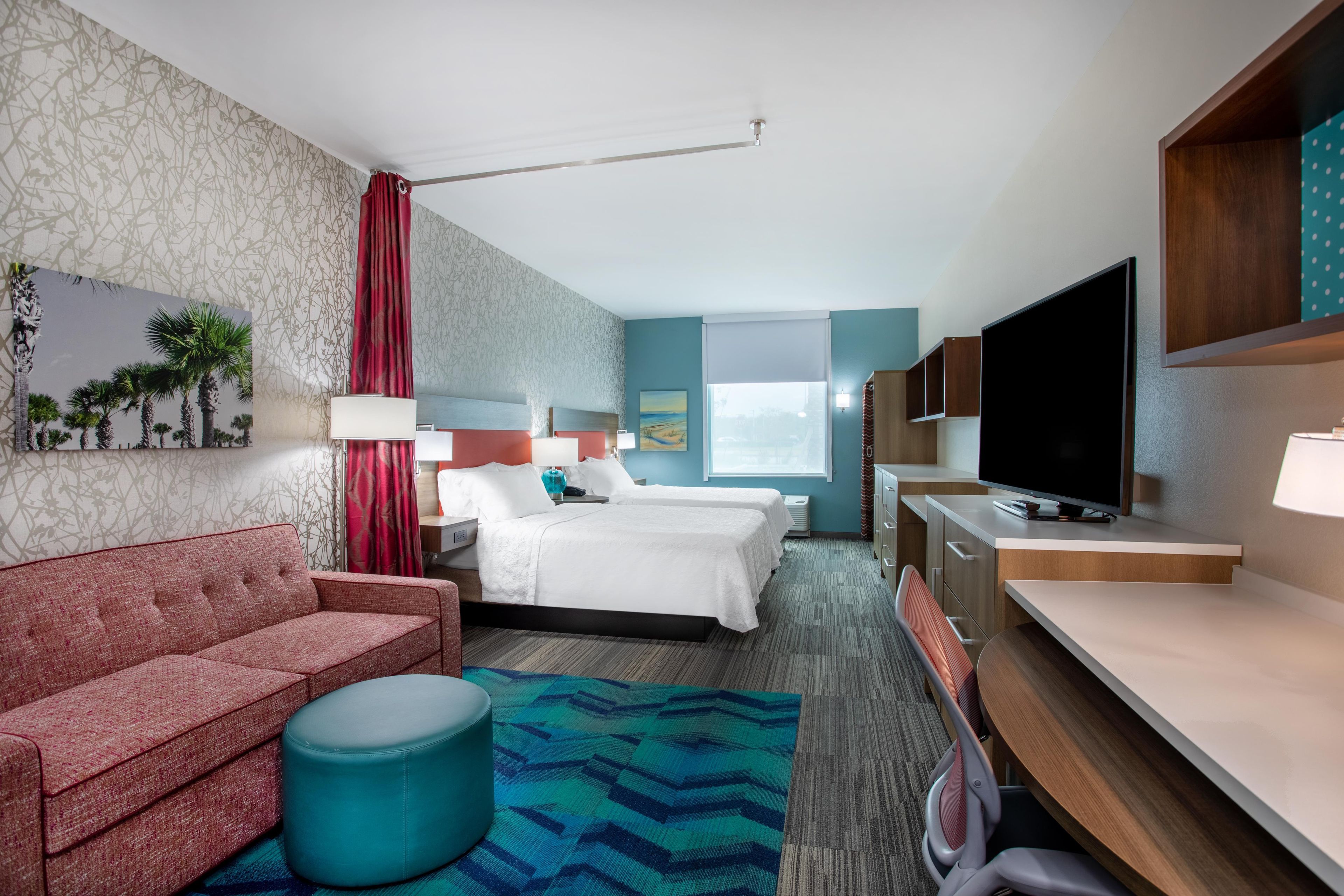 A hotel room with a sofa, two beds, a television, and a desk.