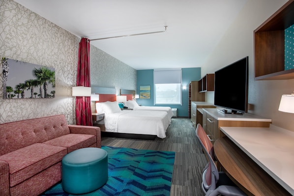 A hotel room with a sofa, two beds, a television, and a desk.