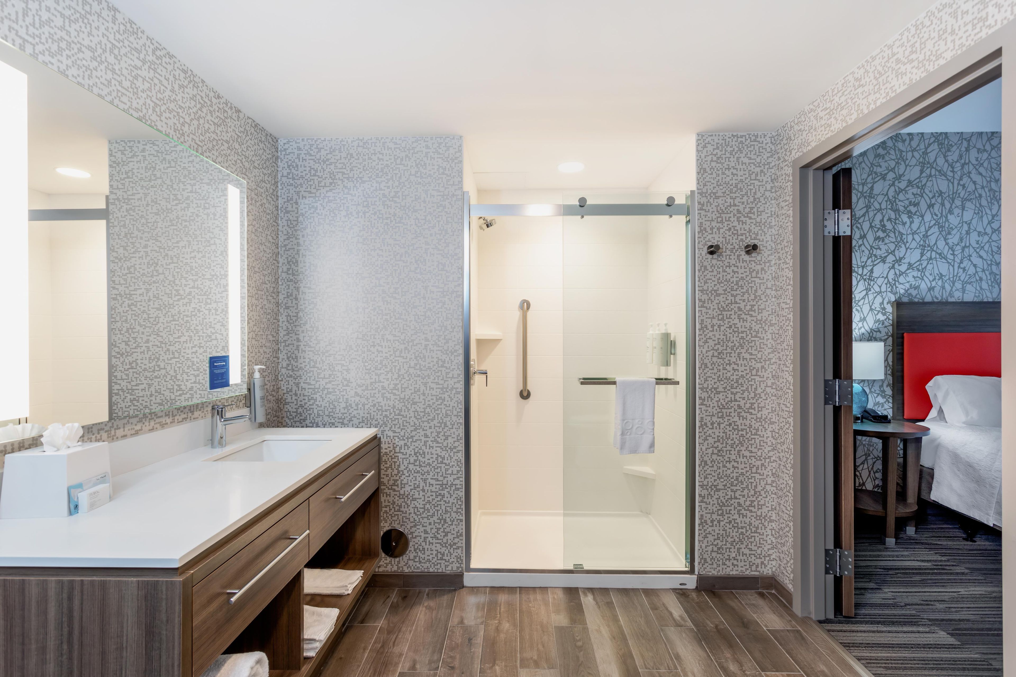 A modern bathroom with a glass-enclosed shower, a vanity with a mirror, and a wooden floor.