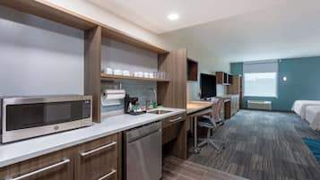 A modern hotel room with a kitchenette, a bed, a desk, and a large window.
