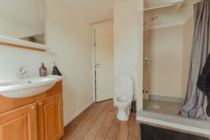 Une salle de bain avec un meuble-lavabo en bois, un lavabo blanc, des toilettes et un espace douche doté d’une porte en verre.