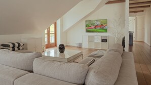 A spacious living room with a high ceiling, a large window, a sofa, a coffee table, and a painting on the wall. - Penthouse - 4BR - Downtown - Harbour (Tórshavn)