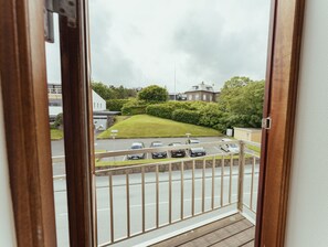Vue depuis un balcon donnant sur un parking où se trouvent plusieurs voitures, une colline herbeuse et un bâtiment en arrière-plan.