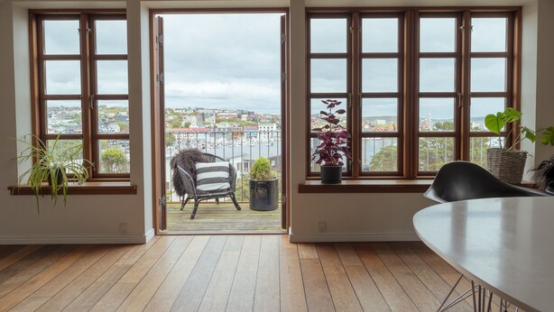 A room with wooden flooring, a dining table, and three large windows with views of a cityscape. - Penthouse - 4BR - Downtown - Harbour (Tórshavn)