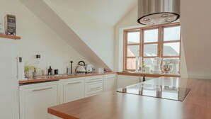 A modern kitchen with white cabinetry, a wooden countertop, and a large window providing natural light. - Penthouse - 4BR - Downtown - Harbour (Tórshavn)