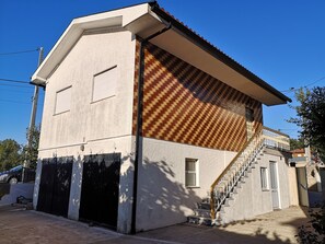 Un edificio de dos plantas con fachada texturizada, una puerta de garaje visible y una escalera que conduce al piso superior.