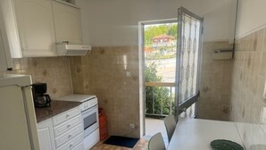 A compact kitchen with white cabinets, a stove, and a dining table. - Appartement F2 Avec Jardin Cloture ET Fleurie (Medelo)
