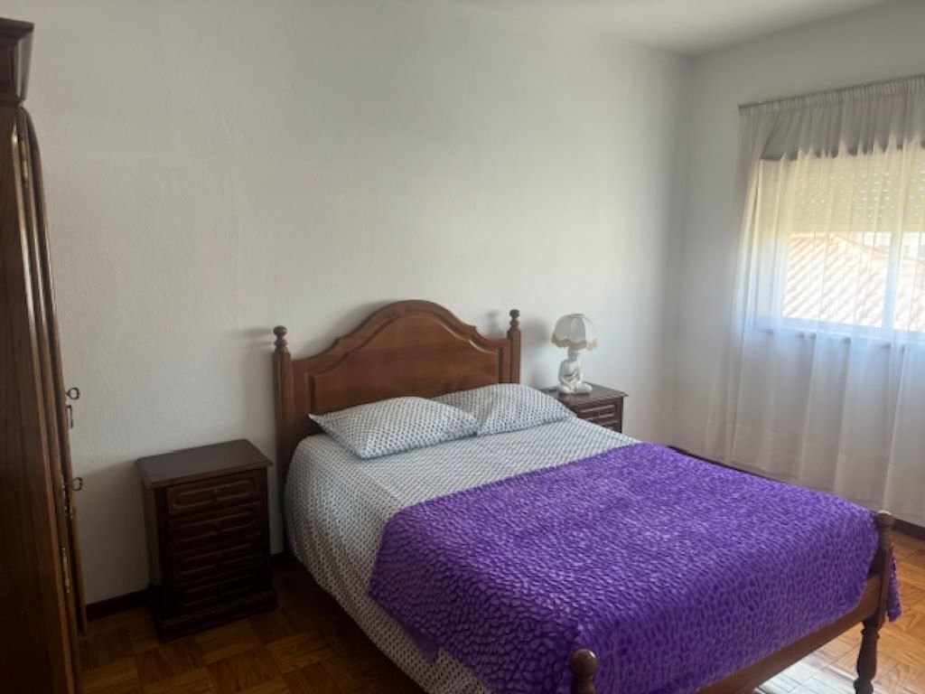 A bedroom with a wooden bed, a nightstand, a dresser, and a window with curtains.