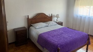 A bedroom with a wooden bed, a nightstand, a dresser, and a window with curtains. - Appartement F2 Avec Jardin Cloture ET Fleurie (Medelo)