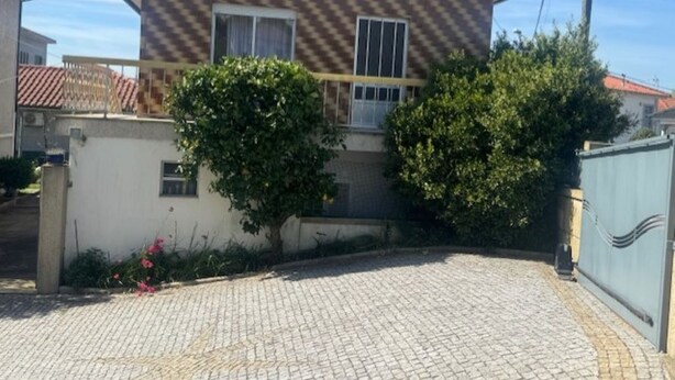 A two-story house with a checkered facade, a covered porch, and a paved driveway. - Appartement F2 Avec Jardin Cloture ET Fleurie (Medelo)