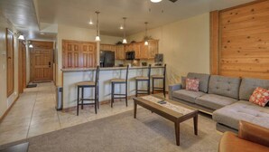 Ein geräumiges Wohnzimmer mit grauem Sofa, einem Couchtisch und einer Küchenzeile mit Holzausbau und einem Barhocker.