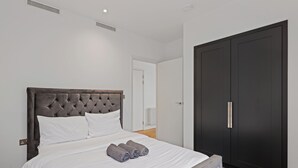 Une chambre à coucher avec un lit doté d’une tête de lit capitonnée, du linge de lit blanc et une pile de serviettes enroulées.