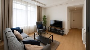 Un salon moderne comprenant un canapé, un fauteuil, une table basse et un téléviseur.