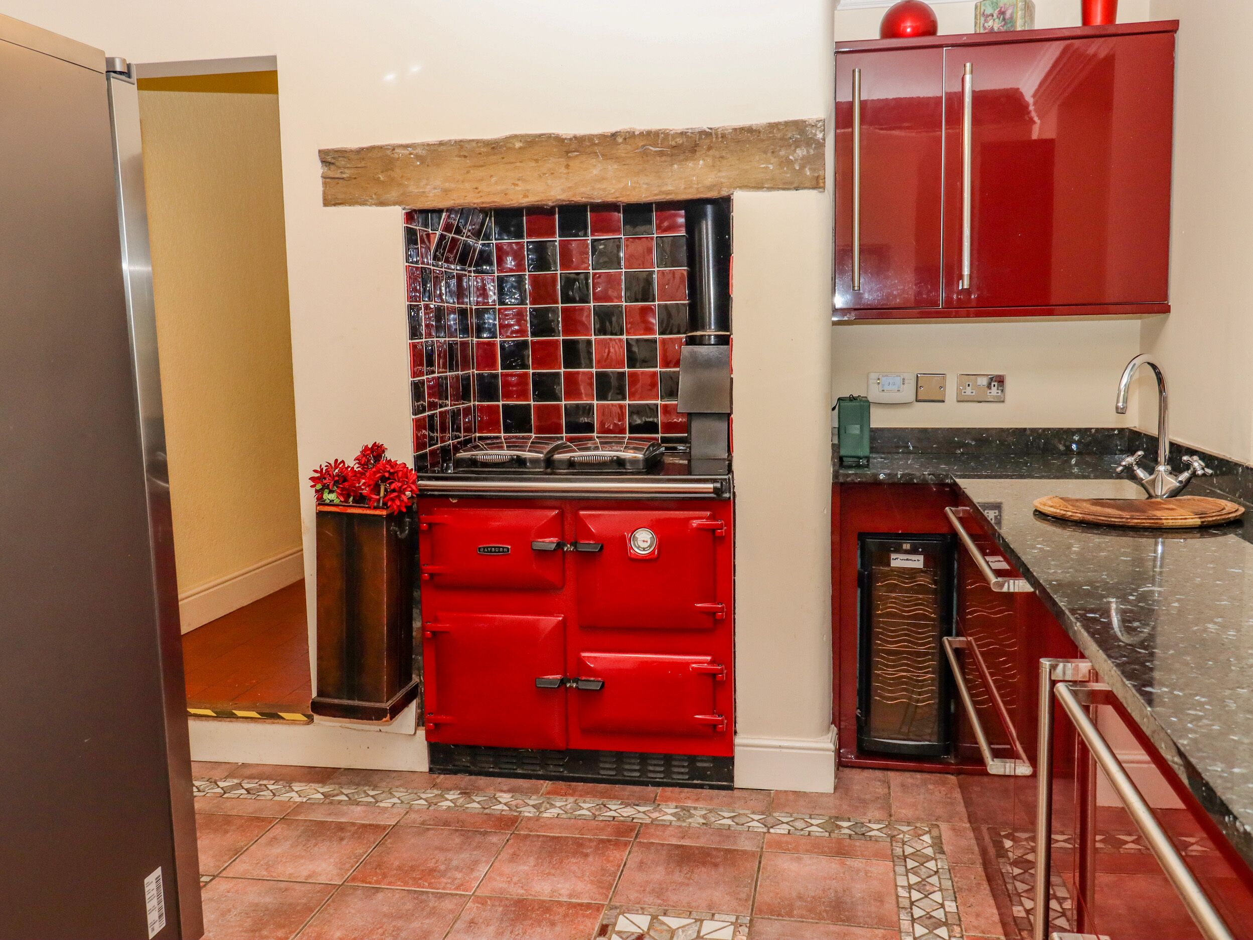 A kitchen with a red stove, a sink with a wooden cutting board, and a red cabinet above the sink.