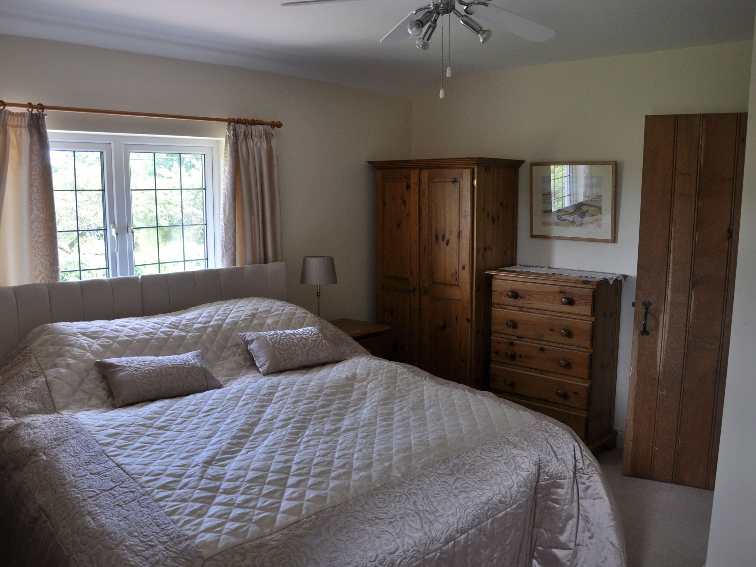 Une chambre avec un grand lit, une armoire en bois et un ventilateur de plafond.