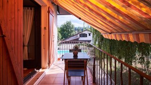 Un balcon avec une table et des chaises en bois, un pot de fleurs et une vue sur une maison et des arbres.