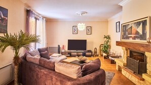 Un salon comprenant un canapé, un téléviseur à écran plat, une cheminée et une grande fenêtre avec des rideaux.