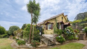 Una casa con una escalera que conduce a la entrada, rodeada de abundante vegetación y una palmera.
