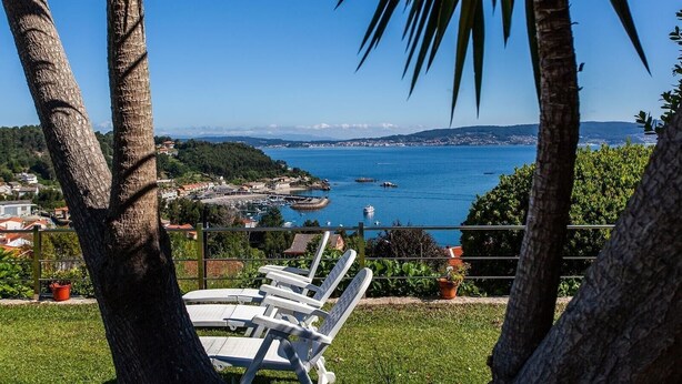 Vista costera con palmeras, un puerto deportivo y sillas de descanso.