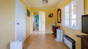 Un pasillo con una puerta blanca, un radiador, un televisor y una ventana con contraventanas blancas.