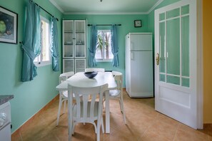 A kitchen with white cabinets, a white refrigerator, a dining table with chairs, and teal curtains.