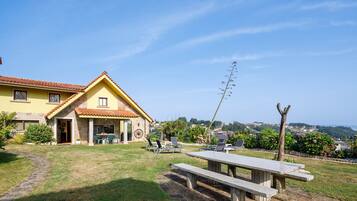 A yellow building with a tiled roof, a patio with chairs, a table, and a view of the landscape.