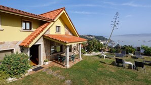 A yellow house with a red-tiled roof, a patio with outdoor furniture, and a view of the sea. - "Casa Nueva de Bueu" with Mountain View, Wi-Fi, Garden & Terrace (Bueu)