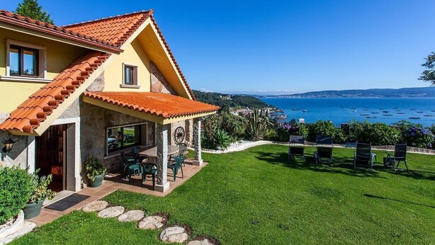 A house with a tiled roof, a patio with chairs, and a view of the sea. - "Casa Nueva de Bueu" with Mountain View, Wi-Fi, Garden & Terrace (Bueu)