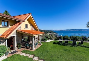 Uma casa com telhado telhado, um pátio com cadeiras e vista para o mar.